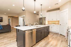 Kitchen with white cabinetry, stainless steel appliances, decorative light fixtures, and an island with sink