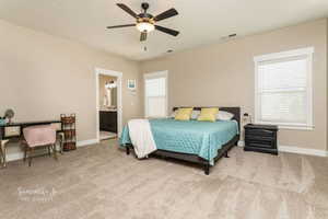 Bedroom with ensuite bathroom, light colored carpet, ceiling fan, and a textured ceiling