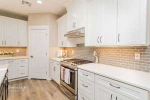 Kitchen featuring white cabinetry, decorative backsplash, stainless steel range with gas cooktop, and light hardwood / wood-style flooring