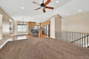 Living room with lofted ceiling, ceiling fan with notable chandelier, and carpet flooring