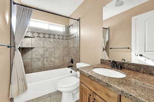 Full bathroom with vanity, tiled shower / bath combo, tile patterned floors, and toilet