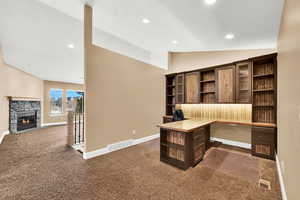 Office area with lofted ceiling, built in desk, and dark carpet