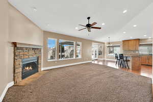 Living room featuring lofted ceiling, a stone fireplace, ceiling fan with notable chandelier, and light carpet