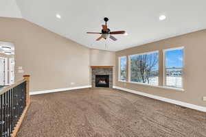 Living room featuring ceiling fan, lofted ceiling, carpet flooring, and a stone gas fireplace