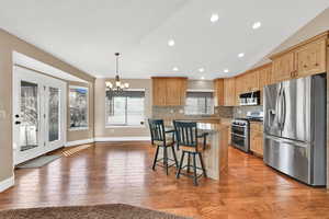 Kitchen featuring a breakfast bar area, vaulted ceiling, hanging light fixtures, a kitchen island, and stainless steel appliances