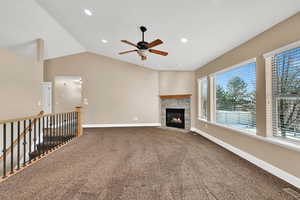 Living room with vaulted ceiling, carpet, ceiling fan, and a fireplace