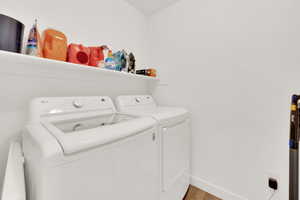 Washroom with washing machine and clothes dryer and wood-type flooring