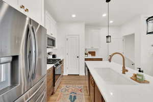 Kitchen with white cabinetry, sink, decorative light fixtures, and appliances with stainless steel finishes