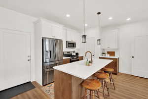 Kitchen with a kitchen island with sink, hanging light fixtures, white cabinetry, and appliances with stainless steel finishes