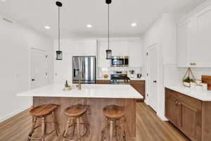 Kitchen with stainless steel appliances, white cabinetry, pendant lighting, and an island with sink