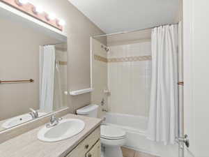 Full bathroom with tile patterned flooring, vanity, toilet, shower / bath combo, and a textured ceiling