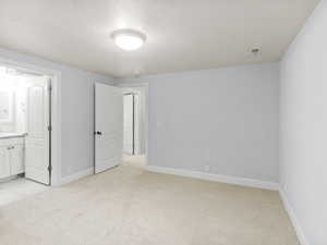 Unfurnished bedroom featuring light carpet, a textured ceiling, and ensuite bath