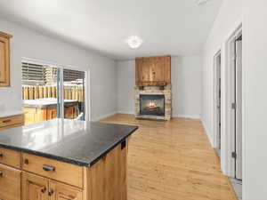 Kitchen with a stone fireplace, light hardwood / wood-style flooring, dark stone counters, and a kitchen island