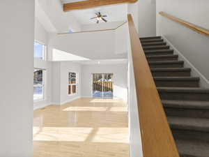 Stairway with a healthy amount of sunlight, beam ceiling, wood-type flooring, and a high ceiling