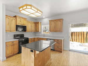 Kitchen with sink, light hardwood / wood-style flooring, black appliances, and a center island