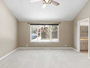 Interior space with ensuite bathroom, vaulted ceiling, light carpet, and ceiling fan