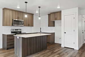 Kitchen featuring stainless steel appliances, a center island, dark hardwood / wood-style floors, and decorative light fixtures