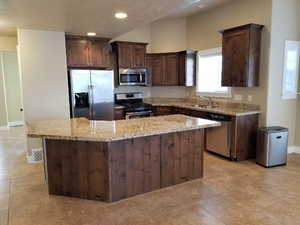 Kitchen featuring light stone counters, stainless steel appliances, a center island, and sink