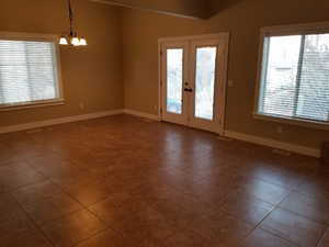 Tiled empty room featuring a notable chandelier and french doors