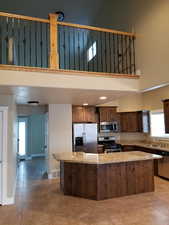 Kitchen with stainless steel appliances, light stone countertops, a kitchen island, and a high ceiling