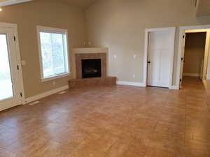 Unfurnished living room featuring lofted ceiling, a fireplace, and light tile patterned flooring