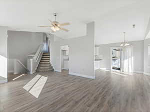 Unfurnished living room featuring high vaulted ceiling, wood-type flooring, and ceiling fan with notable chandelier