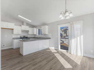 Kitchen featuring vaulted ceiling, dark stone countertops, stainless steel stove, pendant lighting, and white cabinets