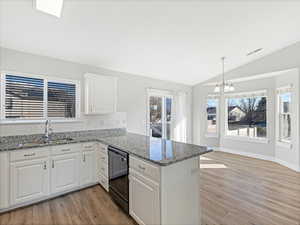 Kitchen with vaulted ceiling, white cabinetry, black dishwasher, sink, and kitchen peninsula