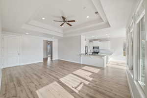 Unfurnished living room featuring sink, a tray ceiling, light hardwood / wood-style flooring, and ceiling fan