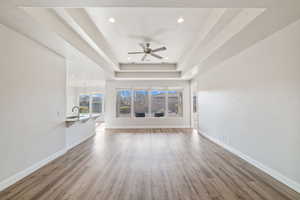 Unfurnished living room featuring sink, a tray ceiling, wood-type flooring, and ceiling fan with notable chandelier