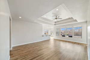 Unfurnished living room with a tray ceiling, wood-type flooring, a textured ceiling, and ceiling fan with notable chandelier