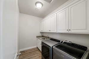 Washroom featuring sink, cabinets, washer and clothes dryer, light hardwood / wood-style floors, and a textured ceiling