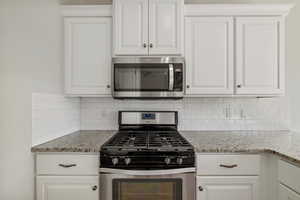 Kitchen featuring white cabinetry, backsplash, light stone counters, and stainless steel appliances