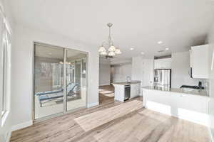 Kitchen featuring decorative light fixtures, a notable chandelier, stainless steel appliances, light hardwood / wood-style floors, and white cabinets