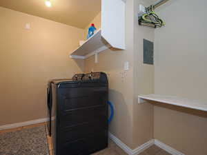 Clothes washing area featuring light tile patterned floors, electric panel, and washing machine and clothes dryer