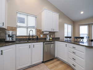 Kitchen with sink, dishwasher, white cabinets, vaulted ceiling, and kitchen peninsula