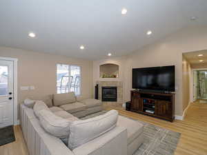 Living room with lofted ceiling, light hardwood / wood-style flooring, and a tile fireplace