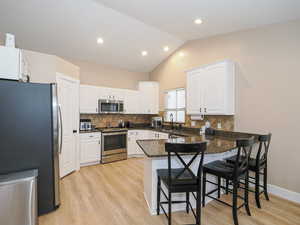 Kitchen featuring white cabinetry, lofted ceiling, a kitchen breakfast bar, kitchen peninsula, and stainless steel appliances