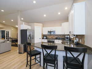 Kitchen featuring lofted ceiling, stainless steel appliances, white cabinets, a kitchen bar, and kitchen peninsula