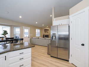 Kitchen featuring stainless steel refrigerator with ice dispenser, dark stone counters, a fireplace, light hardwood / wood-style floors, and white cabinets