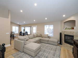 Living room with lofted ceiling, a tile fireplace, and light wood-type flooring