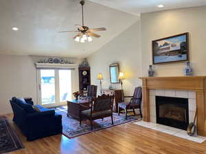 Living room with high vaulted ceiling, a tiled fireplace, ceiling fan, light hardwood / wood-style floors, and a textured ceiling