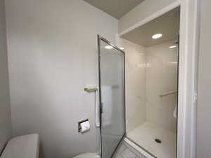 Bathroom featuring a shower with door and toilet