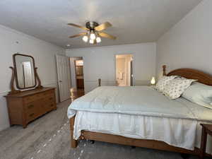 Bedroom with connected bathroom, crown molding, a textured ceiling, ceiling fan, and light colored carpet