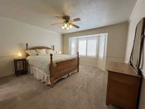 Carpeted bedroom featuring ceiling fan, ornamental molding, and a textured ceiling