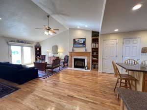 Living room with a tiled fireplace, lofted ceiling, ceiling fan, and light hardwood / wood-style flooring