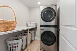 Laundry room with stacked washer / dryer and light hardwood / wood-style flooring