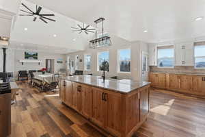 Kitchen with hardwood / wood-style flooring, light stone counters, decorative backsplash, a large island with sink, and a wood stove