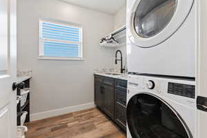 Clothes washing area featuring sink, dark wood-type flooring, cabinets, and stacked washer and dryer