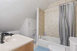 Full bathroom featuring shower / tub combo with curtain, lofted ceiling, sink, toilet, and tile patterned floors